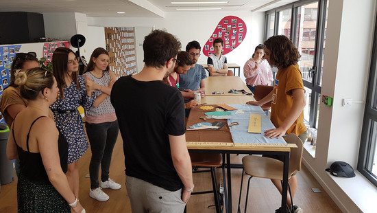 Animation sensibilisation au compostage et au tri des déches organiques par OuiCompost Une séance de sensibilisation de compostage animée par OuiCompost dans les bureaux d'un client. Un groupe de collaborateurs se tiennent autour d'une table pour écouter les explications à propos du tri des déchets alimentaires et le compostage urbain. Sur la table, on voit les photos et les jeux ludiques proposés aux participants de l'atelier.